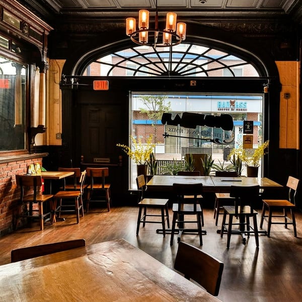 Cozy restaurant interior with wooden tables, brick walls, dark wood paneling, and a large arched window.