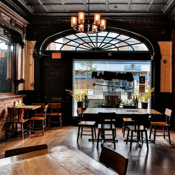 Elegant restaurant dining room with dark wood, exposed brick, and a large arched window.