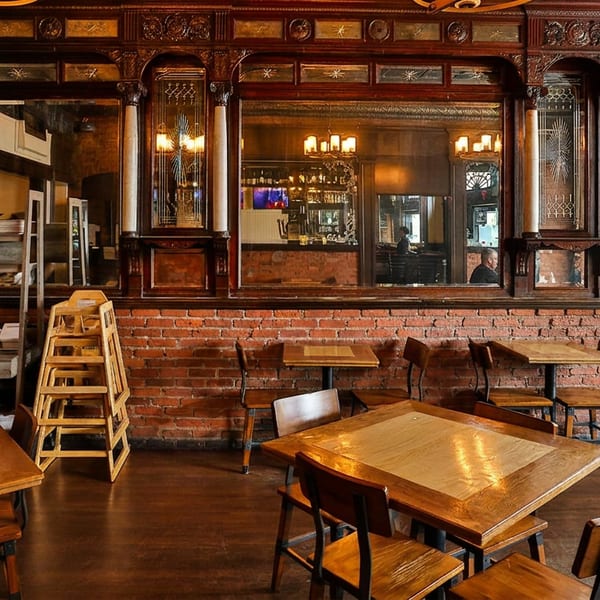 Cozy restaurant interior featuring wooden tables, brick walls, ornate mirrors, and a bookshelf.