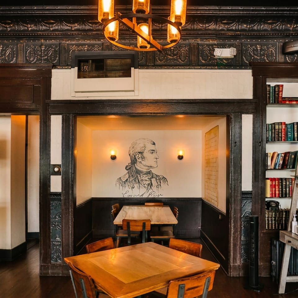Elegant restaurant interior with dark wood, brick, a chandelier, and a mural of a historical figure.