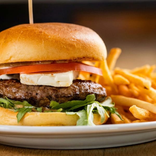 Gourmet burger with feta, tomato, and arugula, served with golden french fries on a white plate.