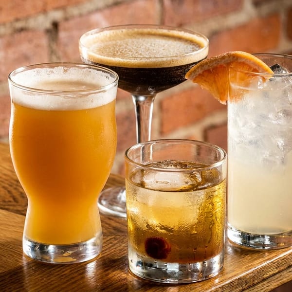 Assortment of beer, dark cocktail, whiskey, and a tall cocktail on a wooden bar.