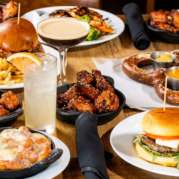 Delicious spread of burgers, fries, chicken wings, a pretzel, and drinks on a rustic wooden table.