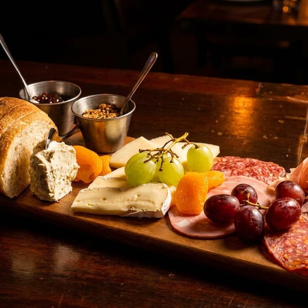 A rustic charcuterie board featuring various cheeses, cured meats, fresh grapes, bread, and condiments.