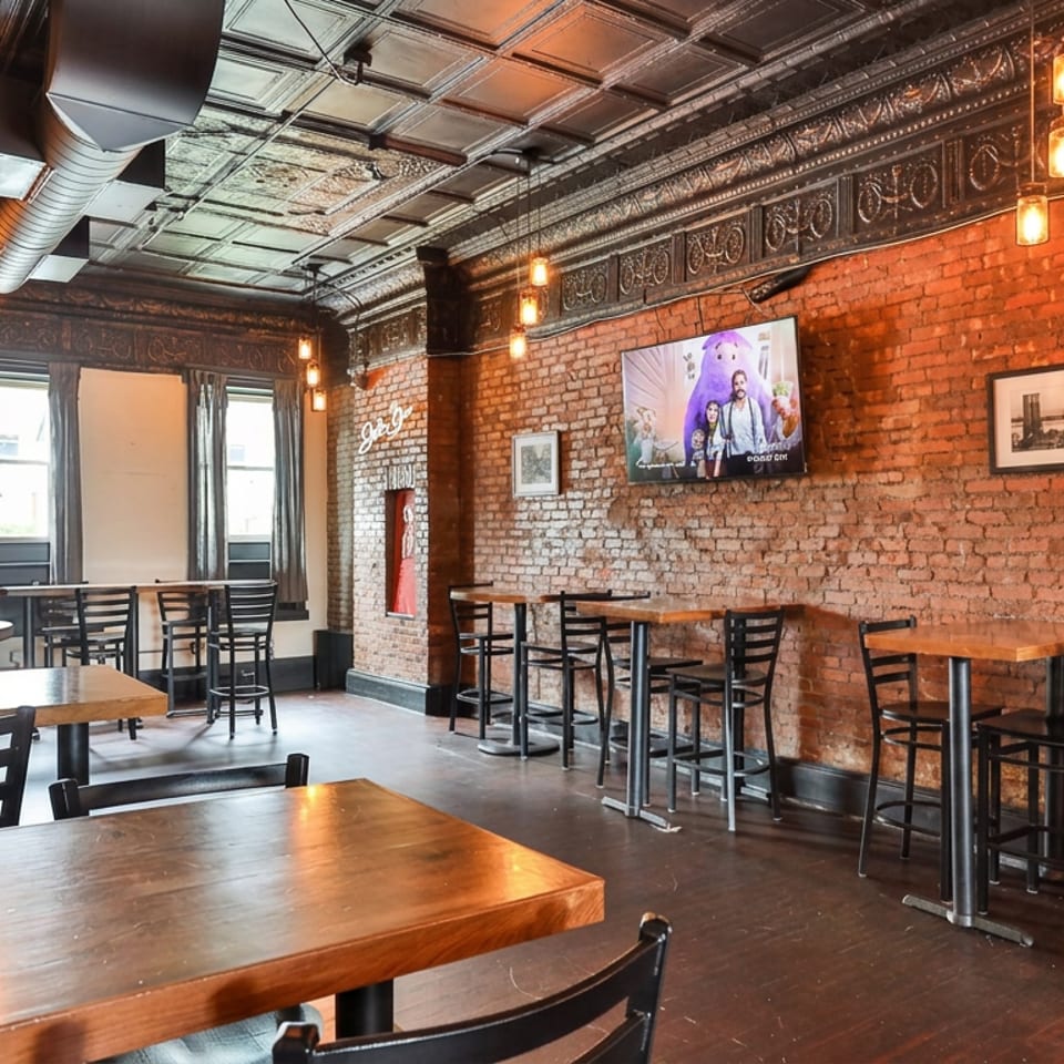 Rustic restaurant interior with exposed brick walls, wooden tables, black chairs, and a TV.